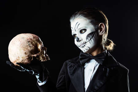 Portrait of a child boy with carnival make-up of a skeleton wearing elegant tail-coat. Studio shot over black background. Halloween. Dia de los muertos. The Day of the Dead.の写真素材
