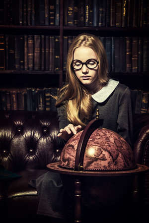 Smart student girl wearing black school dress and glasses is studying at the old library. Fairy vintage style. Education.の写真素材