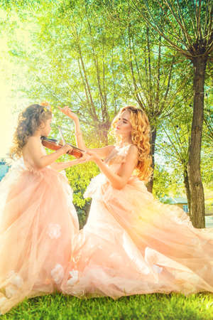 Classical music. Beautiful fairy girl teaches to play the violin a little girl. Musical fairy tales.の写真素材