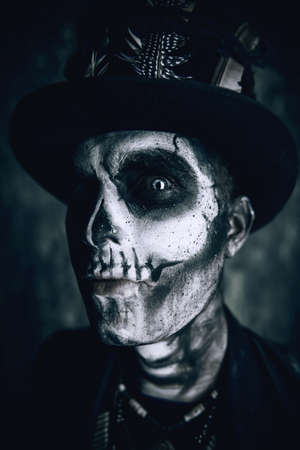 Close-up portrait of a man with a skull makeup dressed in a tail-coat and a top-hat. Baron Saturday. Baron Samedi. Dia de los muertos. Day of The Dead. Halloween.の写真素材