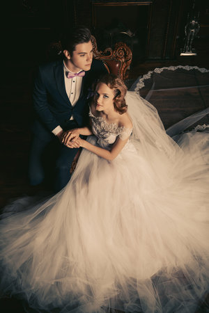 Beautiful bride and groom sitting in tender embrace at a luxurious apartments. Wedding fashion.の写真素材