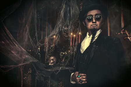 Halloween. Elegant and mysterious gloomy man aristocrat in a black tailcoat and top-hat stands in an old abandoned castle. The Dark Lord. Vampire man.の写真素材