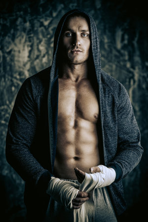 Handsome athletic man in hoodie stands by a grunge wall. Boxer, street fighter.