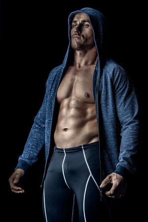 Handsome athletic man in hoodie posing over black background. Sports and bodybuilding concept....