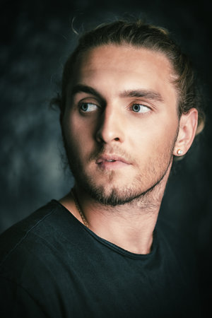 Portrait of a modern young man with long hair. Studio portrait over grunge background. Urban style.
