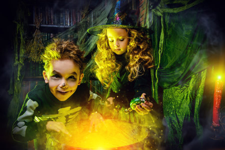 Two funny children in costumes of a witch and a skeleton read a book of spells in a witch's lair....