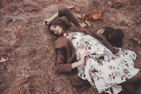 Autumn mood. Beautiful young woman lying on the autumn grass and yellow leaves. Seasonal autumn fashion.の写真素材