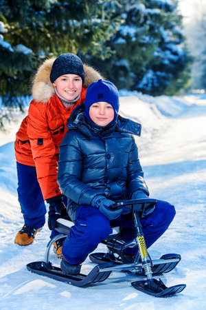 Two happy boys sledding from a hill on a sunny winter day. Snow. Winter clothes. Winter activity.