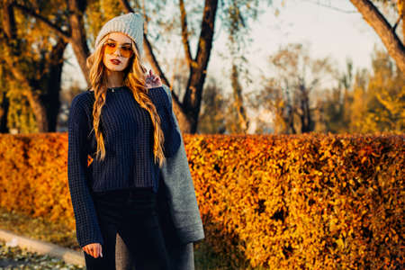 Seasonal autumn fashion. Modern young woman wearing fashionable warm clothes posing in the autumn park.の写真素材