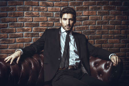 Portrait of a sexy handsome man on a leather sofa. Luxurious lifestyle. Fashion shot. Men's clothing and accessories.の写真素材