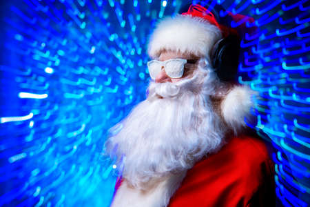 DJ Santa Claus in snowy glasses and headphones. Christmas songs and music. Disco lights in the background.の写真素材