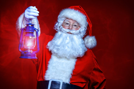 Christmas concept. Portrait of a fairytale Santa Claus holding lantern over red background. Magic time. Copy space.の写真素材