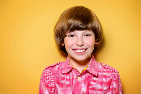 Portrait of a happy smiling boy over bright yellow background. Kid's fashion.の写真素材