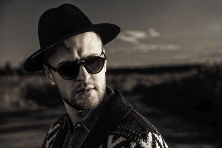 Autumn fashion. Portrait of a handsome man wearing cardigan and hat standing outdoor over autumn nature background.の写真素材