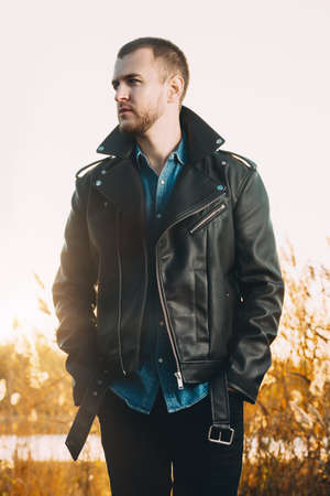 Handsome young man in leather jacket in the autumn park on a sunset. Seasonal fashion.の写真素材