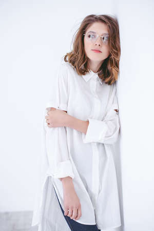 Portrait of a cute girl teenager in spectacles leaned against the white wall. Glasses for a modern young generation. Beauty, fashion.の写真素材