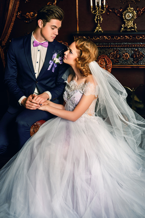 Beautiful bride and groom sitting in tender embrace at a luxurious apartments. Wedding fashion.の写真素材