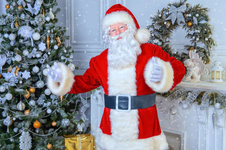 Happy Santa Claus standing by the fireplace and Christmas tree in a beautiful room, decorated for Christmas.の写真素材