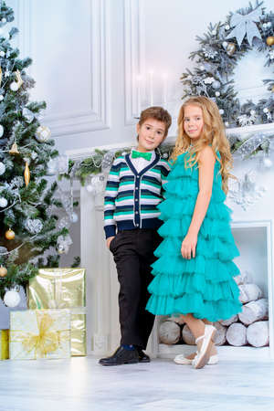 Christmas, fashion concept. Two beautiful children in elegant evening clothes posing by the Christmas tree. Classic luxurious interior decorated for Christmas.の写真素材