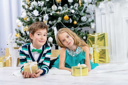 Christmas, fashion concept. Two beautiful children in elegant evening clothes posing by the Christmas tree. Classic luxurious interior decorated for Christmas.の写真素材