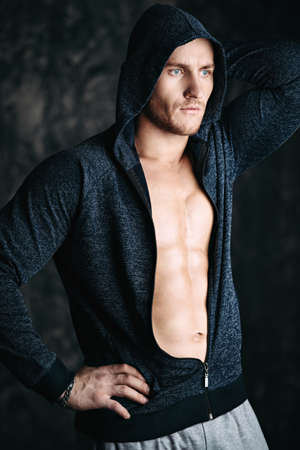 Handsome athletic man in hoodie stands by a grunge wall. Sports and bodybuilding concept. Healthy lifestyle.の写真素材