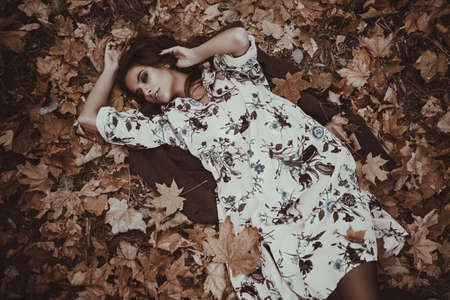 Autumn mood. Beautiful young woman lying on the autumn grass and yellow leaves. Seasonal autumn fashion.の写真素材