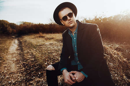 Seasonal autumn fashion. Portrait of a handsome man wearing black coat, a hat and sunglasses. Autumn nature.の写真素材