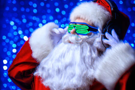 DJ Santa Claus in luminous glasses and headphones. Christmas songs and music. Disco lights in the background.の写真素材
