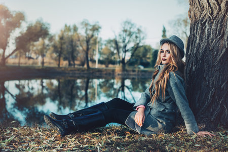 Romantic young woman is sitting under the tree in a beautiful autumn park. Beauty, Autumn fashion.の写真素材