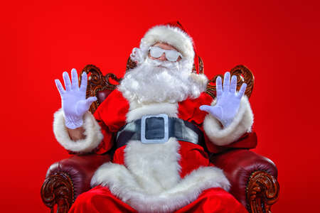 Cool modern Santa Claus in  snowy glasses  sitting in his armchair. Red background. Christmas concept. の写真素材