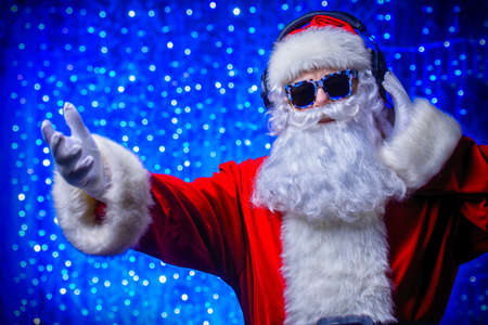 DJ Santa Claus in sunglasses and headphones. Christmas songs and music. Disco lights in the background.の写真素材