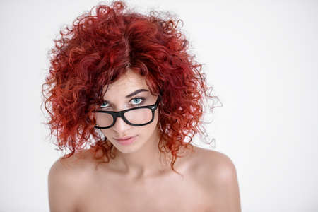 Pretty emotional girl with curly foxy hair looks over the glasses. Beauty cosmetics and hair concept. White background. Copy space.の写真素材