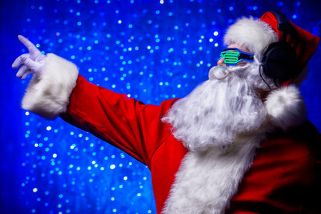 DJ Santa Claus in luminous glasses and headphones. Christmas songs and music. Disco lights in the...