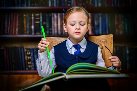 Cute girl looks curiously into the book in a library. Educational concept.の写真素材