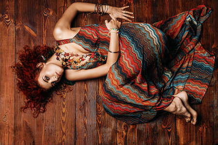 Beautiful bright woman with curly foxy hair wears a dress and beads in boho style. Ethnic style in clothes.の写真素材
