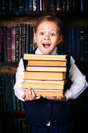 Pretty little girl holds a stack of books in the library and smiling. Educational concept.の写真素材