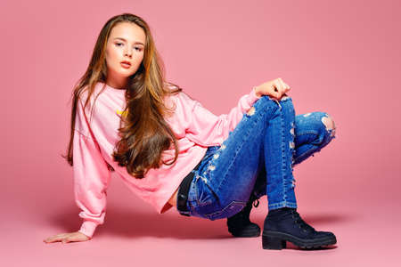 Teen style. Beautiful young model with long hair posing at studio in jeans and pink sweatshirt. Beauty, fashion. の写真素材