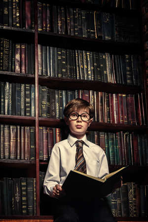 Cute intelligent boy in glasses standing in the old library. Educational concept.の写真素材