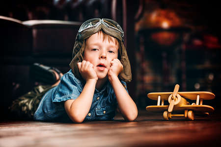 Cute dreamer boy playing with toy airplane at home. Childhood. Fantasy, imagination. の写真素材