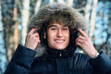 Portrait of a young man in a jacket with a hood. Man stands in winter forest.の写真素材