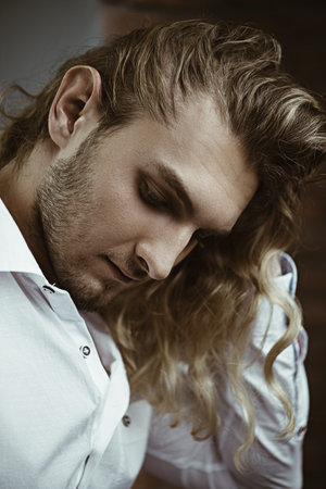 Close-up portrait of a handsome young man with long curly blond hair. Men's beauty, health....