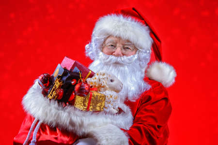 Christmas and New Year concept. Portrait of good old Santa Claus holding a sack with gifts and toys. Red background.の写真素材