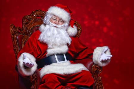 Christmas and New Year concept. Portrait of good old Santa Claus sitting in his armchair. Red background.の写真素材