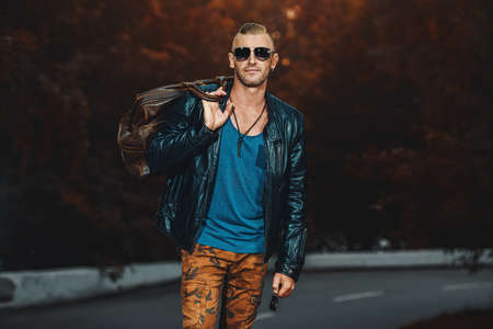 Handsome brutal man in leather jacket walking down the road. Biker man is going to trip. The spirit of independence.の写真素材