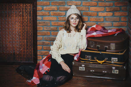 Modern hipster girl wearing glasses and knitted clothes in a room with brick walls. Loft style interior. Teenager girl in warm clothes.の写真素材
