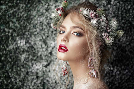 Close-up portrait of a beautiful young woman with christmas tree in hairstyle and holiday make-up over snow-covered green background. Beauty, fashion.の写真素材