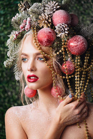 Portrait of a beautiful young woman with christmas tree in hairstyle decorated with beads and balls. Holiday make-up. Beauty, fashion.の写真素材