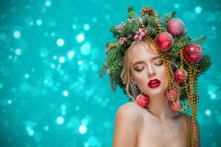Portrait of a beautiful young woman with christmas tree in hairstyle decorated with beads and balls over blue background. Holiday make-up. Beauty, fashion.の写真素材