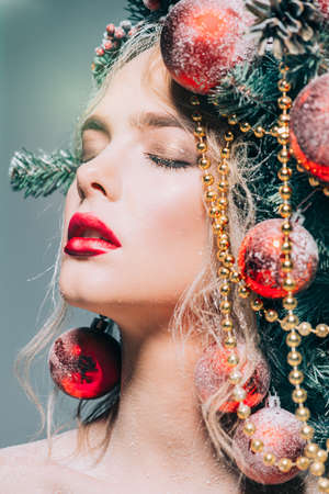 Close-up portrait of a beautiful young woman with christmas tree in hairstyle decorated with beads and balls. Holiday make-up. Beauty, fashion.の写真素材