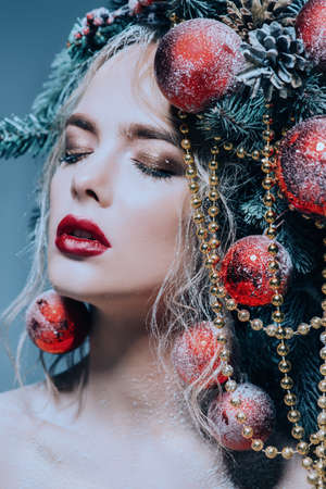 Close-up portrait of a beautiful young woman with christmas tree in hairstyle decorated with beads and balls. Holiday make-up. Beauty, fashion.の写真素材